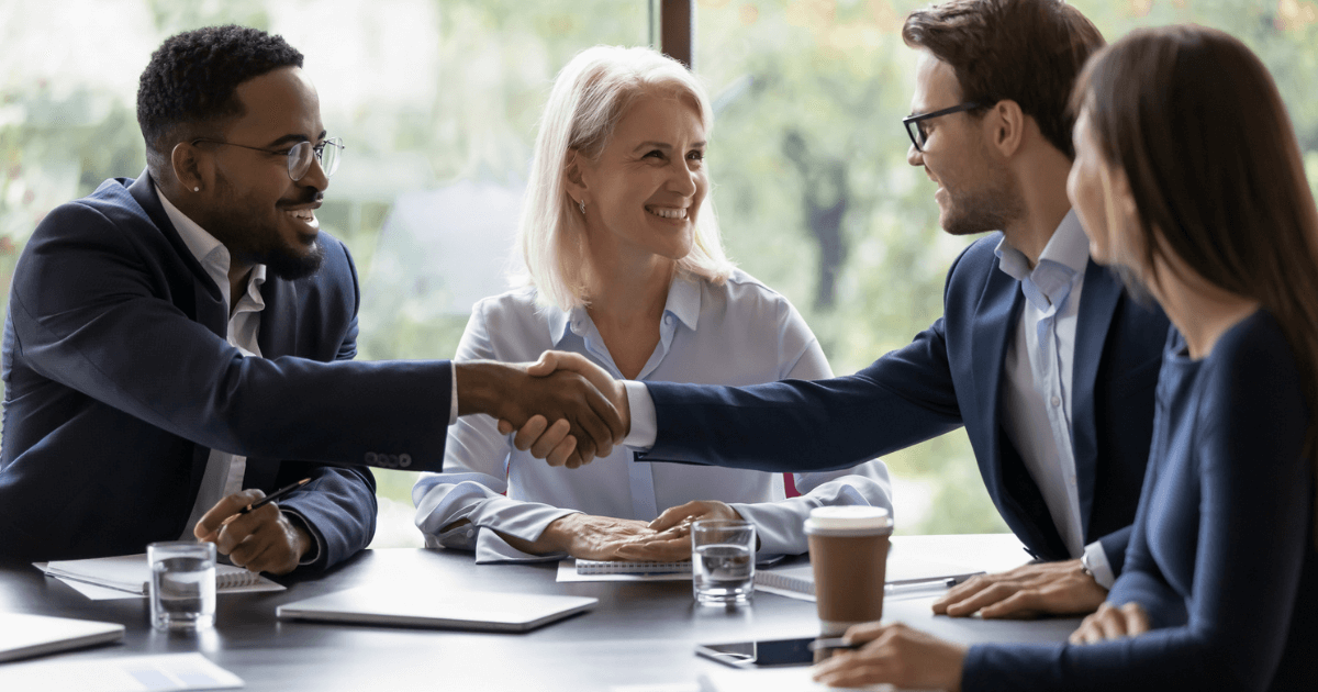 Group gathered at a business table and two gentlemen shaking hands over senior living acquisitions.