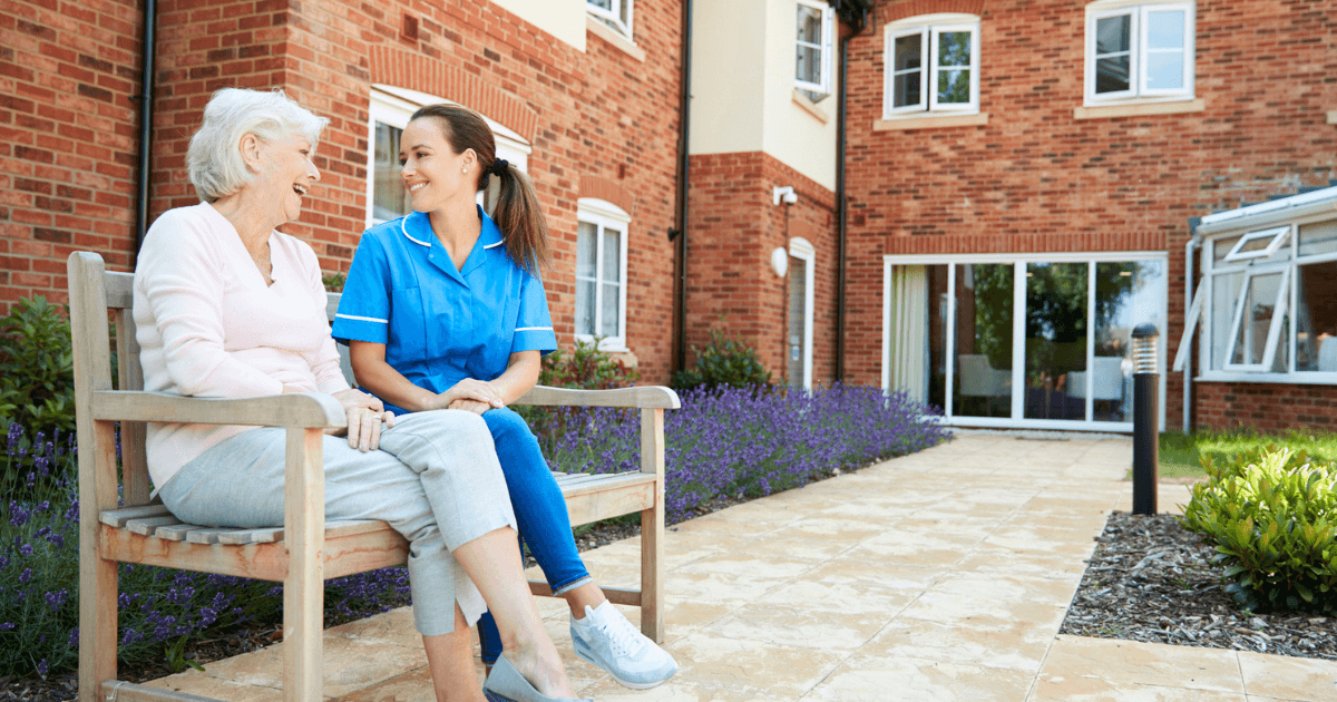 Two adult women sitting on a bench outside.